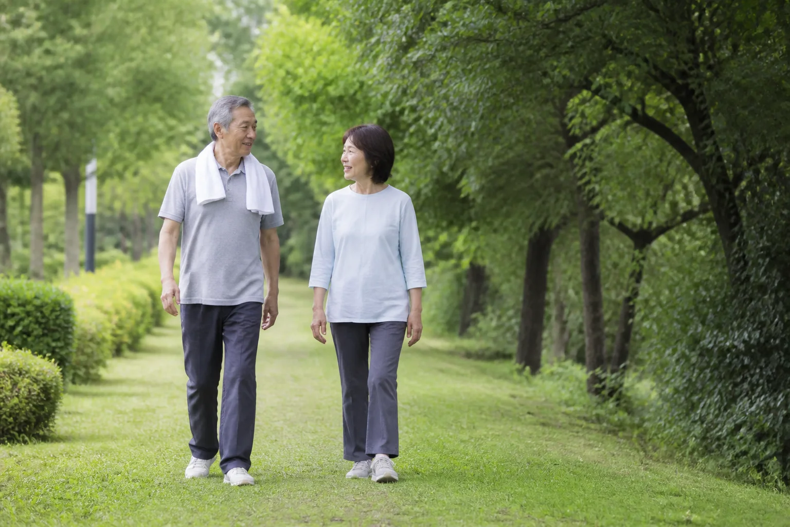 緑の公園を自然なペースで歩く日本人の夫婦