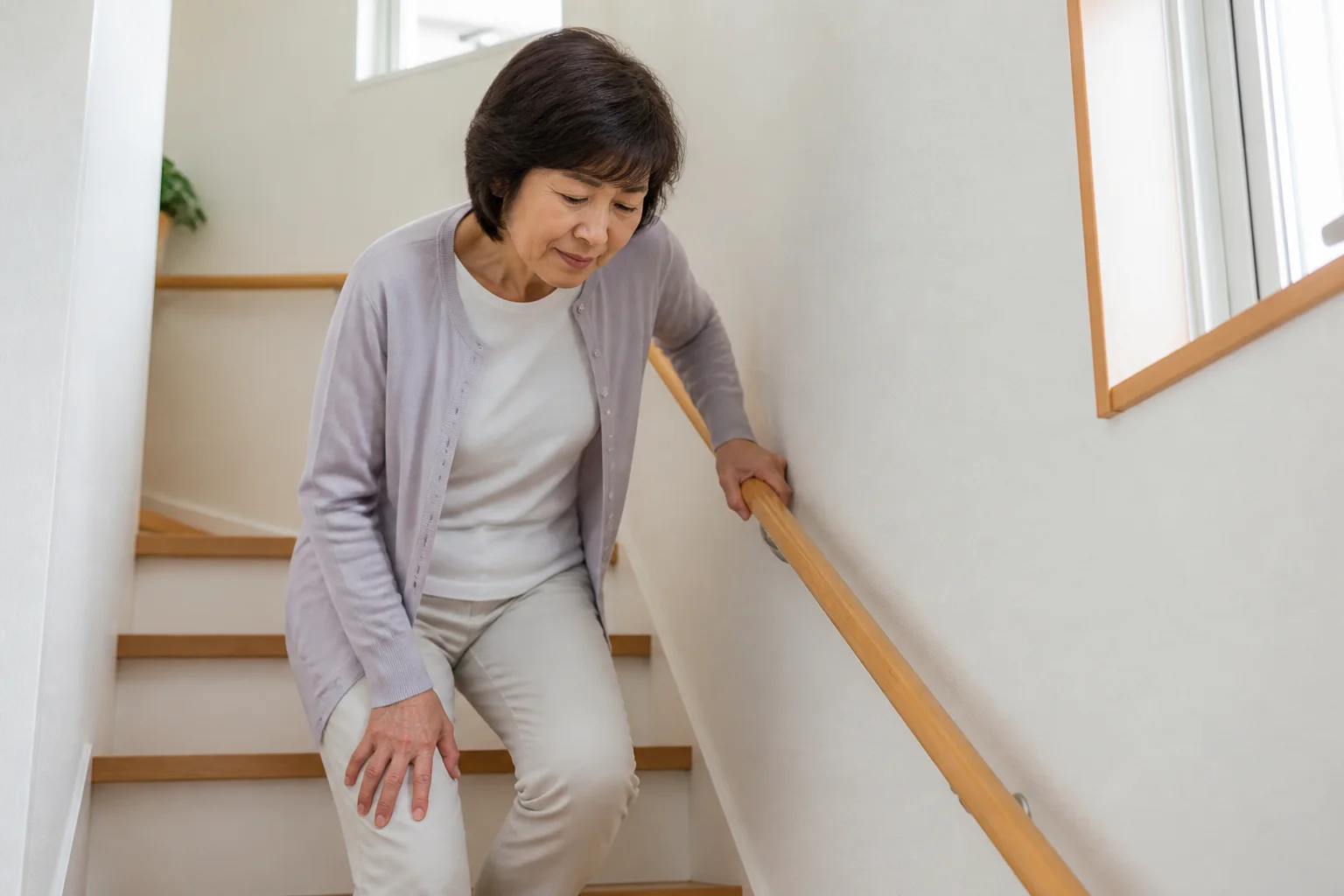 階段で膝の痛みを感じて手すりを使う患者さん
