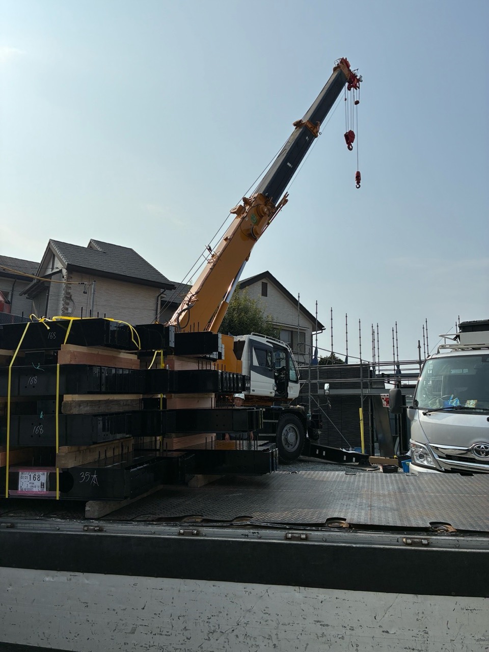 鉄骨を積んだ車両の横で作業する建築用クレーン